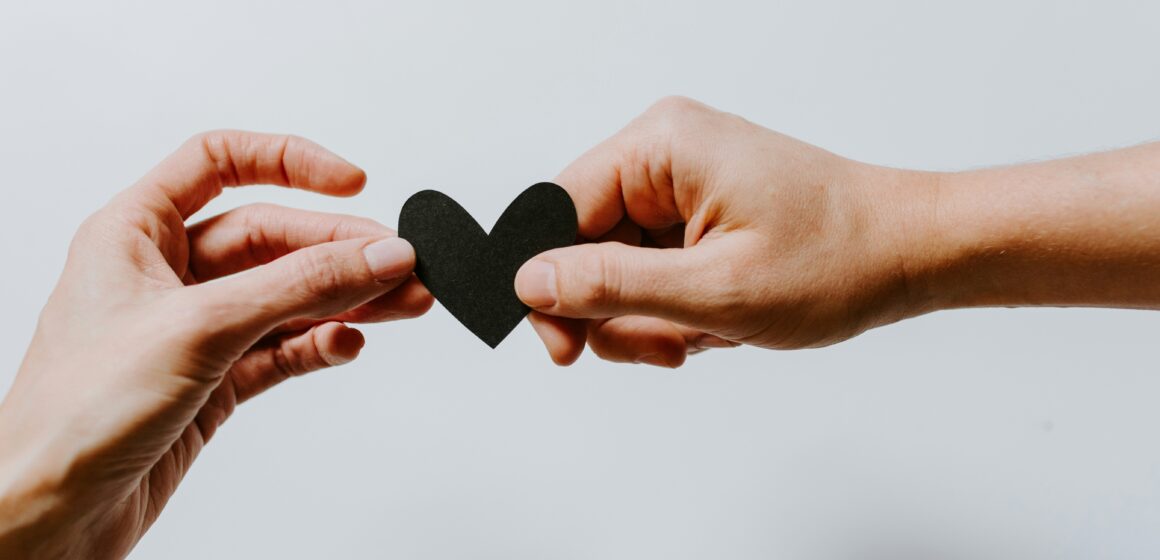 Two hands gently holding a small black paper heart between them, symbolising connection and a healthy relationship.
