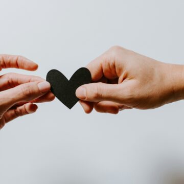 Two hands gently holding a small black paper heart between them, symbolising connection and a healthy relationship.