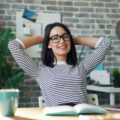 Relaxed woman leaning back at her desk with hands behind her head, symbolising calm productivity.