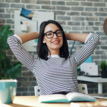 Relaxed woman leaning back at her desk with hands behind her head, symbolising calm productivity.